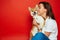 Woman in white t shirt and jeans holding and embracing Shiba Inu dog on plane red background. Love to the animals