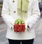 Woman in white wool coat holding Christmas gift present with festive wrapping paper and bow. Holiday gifts presents background