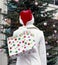 Woman in white wool coat and santa hat holding shopping bag with Christmas tree in background. Holiday giving Christmas shopping