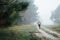 Woman in wide-brimmed felt hat and authentic poncho going along the forest at foggy morning