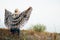 Woman in wide-brimmed felt hat and authentic poncho standing in high brown grass at foggy morning