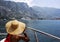 Woman in a wide-brimmed straw hat sits in boat and looks at the sea and mountains. Back view.