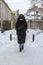 woman in winter coat walking by city street after snowstorm