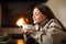 Woman in winter drinking coffee beside a fireplace