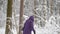 Woman in winter jacket with hood walking with difficulty through winter forest