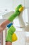 A woman wipes yellow cloth kitchen cabinets, applying the chemical with a bottle. Cleaning of the apartment