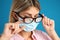 Woman wiping foggy glasses caused by wearing disposable mask on blue background, closeup. Protective measure during coronavirus