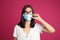 Woman wiping foggy glasses caused by wearing disposable mask on pink background. Protective measure during coronavirus