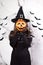 A woman in a witch costume in a hat holds a bucket of candy instead of a head. Halloween people vertical photo.