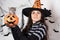 A woman in a witch costume in a hat holds a bucket pumpkin with cat. Halloween people and animal.