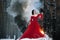 Woman witch in red dress and with raven in her hands in snowy forest.