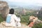 Woman withTibetan terrier dog sitting on the edge of a cliff overlooking Meteora valley