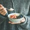 Woman in woolen sweater eating rice coconut porridge, square crop