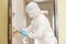 Woman worker disinfects door handles of house from infection with virus and microbes in biochemical suit. Coronavirus