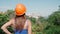 Woman worker in a hard hat on the background of the city on summer sunny day. Girl trainee builder getting ready to start working