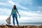 The woman worker stands on the shore of the sea. She holds a garbage bag in one hand and a dirty bottle in the other. The