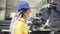 Woman-worker in yellow and transparent protecting glasses, hard hat and mask inspect equipment on recycle plant. Press