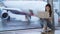 Woman working on laptop near window at airport, blurred airplane on background