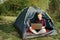 Woman working on laptop in tent in nature.
