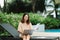 A woman working at the swimming pool with her laptop computer holding paperwork in her hand. It is imperative for young Asian