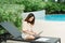 A woman working at the swimming pool with her laptop computer holding paperwork in her hand. It is imperative for young Asian