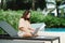 A woman working at the swimming pool with her laptop computer holding paperwork in her hand. It is imperative for young Asian