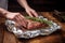 Woman wrapping meat with rosemary. Generate Ai