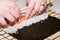 Woman wrapping rice and salmon to sushi roll