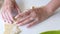 A woman wraps blueberries in a dough that are lying on a rolled dough. A woman forms dumplings with a glass