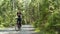 Woman in wreath of daisies riding bike alone in the bright green forest and looking around