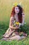 Woman in wreath with red hair sits in grass of field a