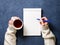 woman writes in notebook on dark blue table, hand in shirt holding a pencil, cup of tea, sketchbook drawing, top view