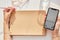 Woman writes using her left hand on a vintage crafting paper and holding a phone. Glasess and glass of water. Conceptual