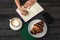 Woman writing down ideas to the notepad sitting in a French cafe. Croissant and a cup of cappuccino on a black wooden table