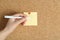 Woman writing on sticky note pinned to corkboard, closeup