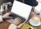 Woman writing text on open laptop on wood table with empty blank screen monitor at home, person drink cup of coffee on background