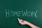 Woman writing word HOMEWORK on chalkboard, closeup