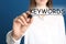 Woman writing word KEYWORDS on transparent board against background, closeup