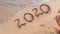 Woman writting 2020 on sand beach. ocean wave and lettering on the beach. Happy New Year 2020. tropical vacation good bye