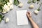 Woman writting or planning checklist on blank of white roses on grey. Top view, copy space
