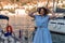 Woman yacht sea. A young happy woman in a blue dress and hat stands near the seaport with luxury yachts. Travel and