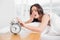 Woman yawning while extending hand to alarm clock