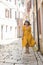 woman in yellow dress with bit straw hat walking by old tourist city in croatia