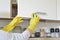 Woman in yellow gloves washes the door in kitchen cabinet