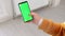 A woman in a yellow knitted sweater with a smartphone and a green phone screen swipes her finger across the screen. The