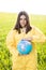 A woman in a yellow protective suit stands in the middle of a green field holding a globe. The concept of saving the planet from