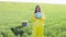 A woman in a yellow protective suit stands in the middle of a green field and holds a globe in her hands, next to a garbage can