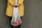 Woman in a yellow raincoat carrying string bag with fresh bananas and apples on the street against brown wall