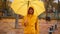 woman in yellow raincoat with umbrella walks at rainy autumn day in city park with attractions for children. wet fallen