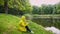Woman in yellow raincoat using phone sitting in summer park. Girl walking admiring lake landscape view